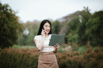 A confident young Asian woman is working on her laptop in a vibrant park. E-banking and career aspirations in a modern lifestyle.