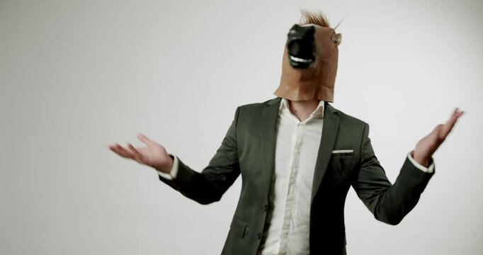 A man in a suit dances while wearing a horse mask. The mask moves with his head, and his arms flail open in surprise and excitement. The background is solid white.
