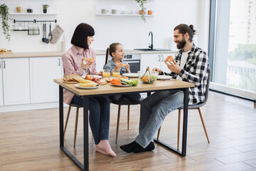 Caucasian family with adult couple and child eating pizza for breakfast in modern kitchen. Family bonding, happiness, and home meal concept with bright and minimalist decor.