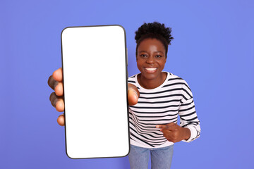 Happy woman pointing at mobile phone with blank screen on violet blue background. Mockup for design