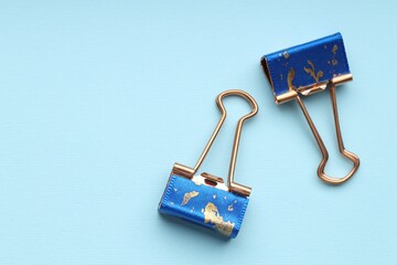 Two binder clips on light blue background, flat lay. Space for text