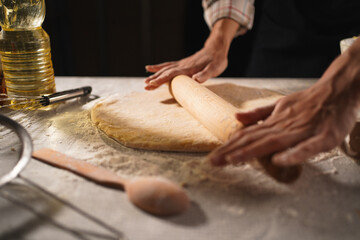 Woman rolling out dough with roll pin on kitchen table, close-up