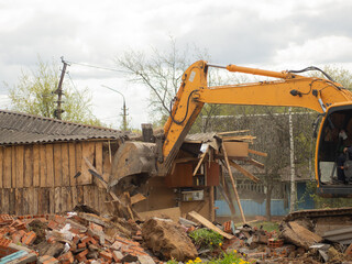 Fototapeta premium yellow excavator demolishes old buildings with its bucket