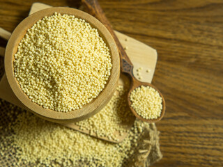 Raw organic millet groats in bowl with wooden spoon on rough napkin and wooden background