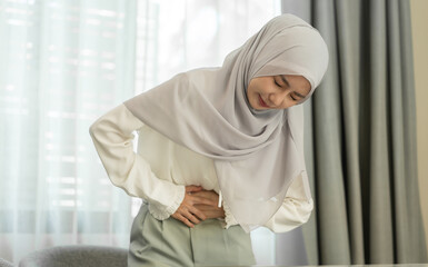 Muslim woman experiencing stomach pain, health discomfort, digestive issues, abdominal cramps,...