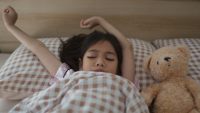 Little asian girl wakes up and stretching on bed in morning, Health care and good morning world concept