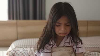 Naklejka premium The scared little girl in the bedroom crying with her hands holding her teddy in fear of monsters in darkness in the bedroom in the Child's nightmares imagination and psychological distress concept.