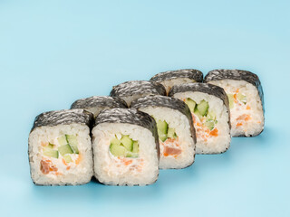 Studio photography of Maki roll with cucumber and salmon mousse wrapped in nori. Isolated on solid light blue background