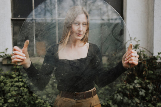 Woman holding round glass pane and standing in backyard