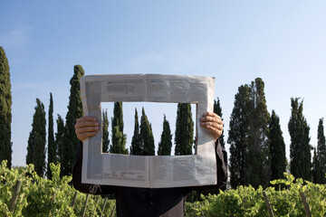 Italy, Tuscany, invisible man surrounded by cypresses reading newspaper with a hole
