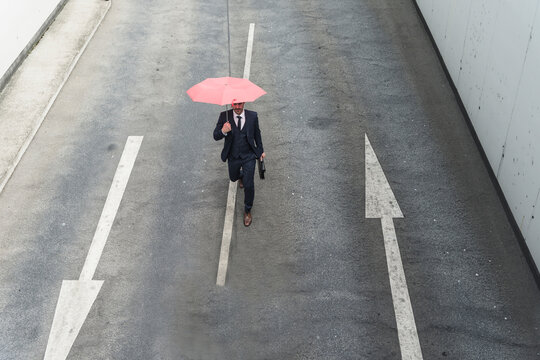Businessman with umbrella walking on road with arrow signs