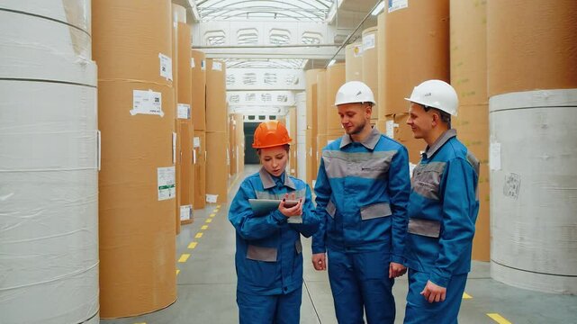 Warehouse inspection, paper industry, production of ecological biodegradable packaging from recycled materials. Group of paper mill workers engineers take inventory of huge warehouse with rolls paper