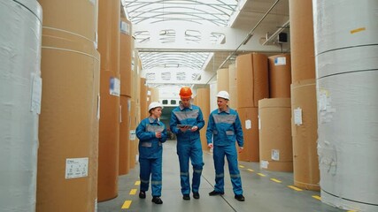 A group of paper mill workers conduct an inspection of a huge paper warehouse. Workers collect data and enter it into a digital tablet. Packaging industry, production of packaging from recycled paper - Powered by Adobe