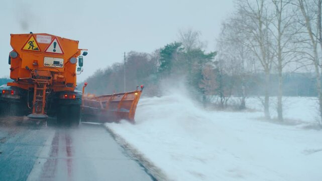Snowplow clears road of snow after a snowfall, salting street in winter time, snow removal. A snow plow truck clears snow from the road, side of road after a snowstorm and blizzard. Road maintenance