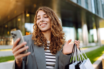 Happy woman using smartphone while enjoying a day shopping. Black Friday, sale and discount. Buying clothes presents for holidays.