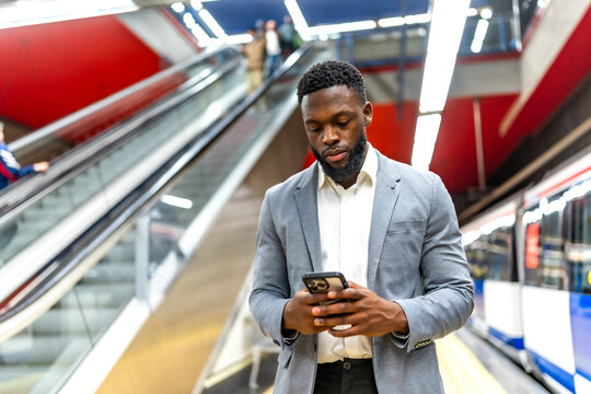 Businessman using smartphone in subway station with escalator in background
