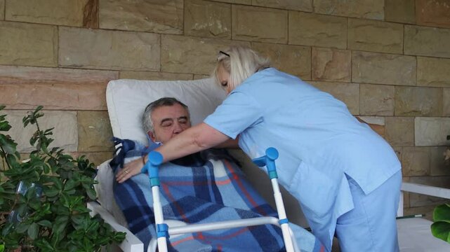 Nurse covering elderly man in wheelchair with blanket