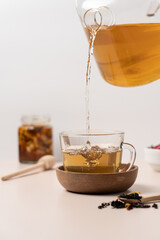 Tea pouring into glass cup from teapot on light background with copy space. Cup of freshly brewed fruit and herbal tea