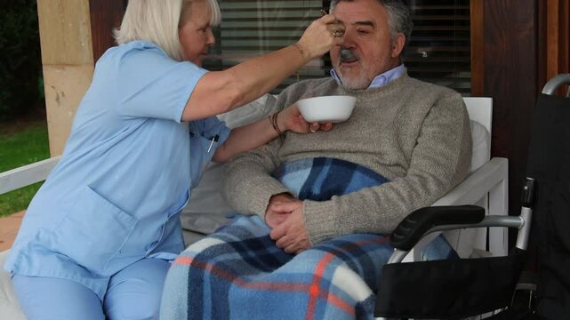 Nurse assisting elderly man in wheelchair eating