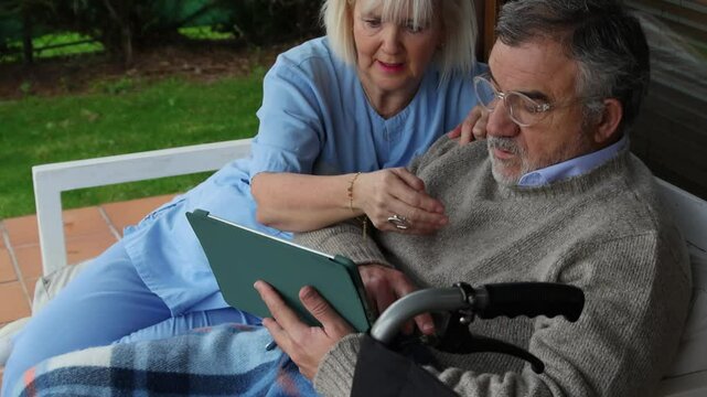 Nurse assisting elderly man in wheelchair using digital tablet
