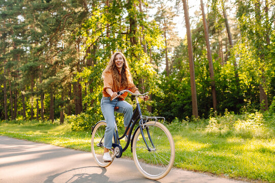 Happy woman riding bicycle bike on sidewalk in city green park outdoors. Active lifestyle concept.