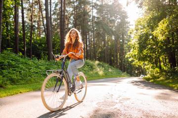 Happy woman riding bicycle bike on sidewalk in city green park outdoors. Active lifestyle concept.