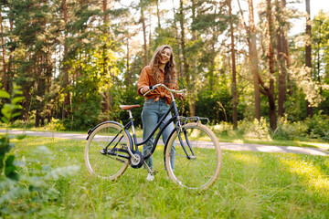 Happy woman riding bicycle bike on sidewalk in city green park outdoors. Active lifestyle concept.