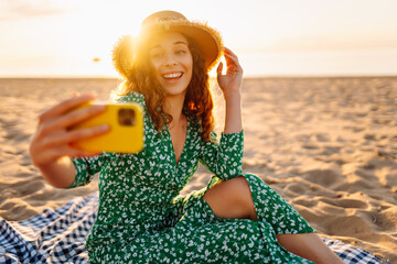 Happy woman do selfie shot mobile cell phone post photo on social network sits rest on sea ocean sand shore beach seaside in summer day. Lifestyle concept.