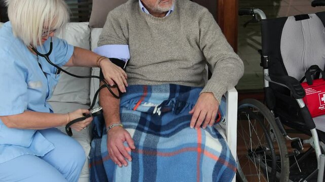 Nurse measuring blood pressure of elderly man in wheelchair