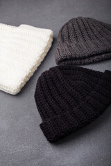 Three knitted woolen beanie caps or hats on wooden background, white black and grey. Flat lay, vertical shot. Knitwear