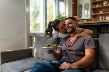 Woman shares tender moment with her partner, delivering homemade breakfast and a loving kiss in cozy living room.