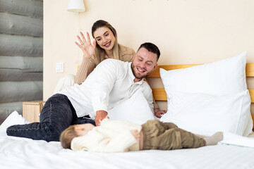 Fototapeta premium Family having fun in cozy room. A joyful family shares tender moments in their warm bedroom while their child plays on the bed.