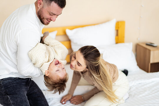 Family joy during playtime in a bedroom. A joyful family shares playful moments; a dad lifts his laughing child while the mother watches with love.