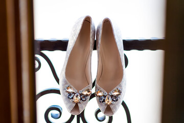 Silver heels on balcony railing. Sparkling silver shoes with jeweled accents rest on a decorative balcony railing during daylight hours.