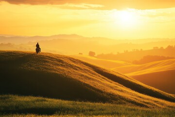 Fototapeta premium A lone rider perched on a grassy hill at sunrise, enjoying the beauty of nature as golden rays flood the scene with warmth and light.