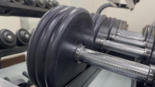 The image shows a close-up of several dumbbells on a rack in a gym, the weights are black and silver, ready for a workout or training session. It depicts fitness and training.