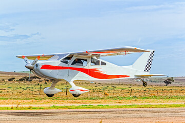 White and red high wing home-built single engine kit aircraft with four seats and fixed undercarriage taking off from an airstrip in the Western Cape, South Africa
