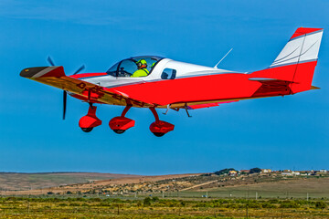Low flying bright red two-seater single engine aircraft at a small airfield in the Western Cape,...