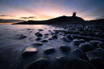Dunstanburgh Castle sunrise on the rocky Embleton Bay, Northumberland, UK.