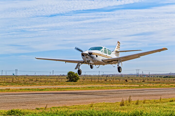 Sleek single engine four seat aircraft with high rear stabilizer and retracting undercarriage taking off from an airstrip in the Western Cape, South Africa