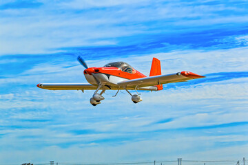 Bright red and white kit aircraft with fixed tricycle undercarriage flying against a blue cloudy sky in the Western Cape, South Africa