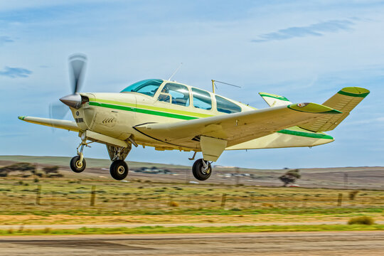 Light aircraft six-seat with green stripes and retracting undercarriage and unique V shaped tail taking off from an airstrip in the Western Cape, South Africa