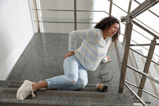 Woman with injured back on stairs in building after fall. Dangerous accident
