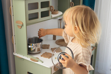 cute toddler blonde baby girl playing on toy kitchen at home,