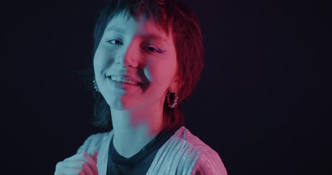 Beautiful Asian girl dancing looking at camera in neon light on dark background. Disco party and entertainment concept.