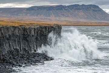 Dramatic coastal scene with crashing waves against rocky cliffs and a distant mountainous backdrop
