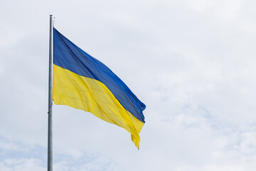 Ukrainian waving flag high pillar national symbol of independent country in war, neutral gray sky background