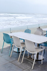 Seaside patio with empty blue and white chairs overlooking ocean waves