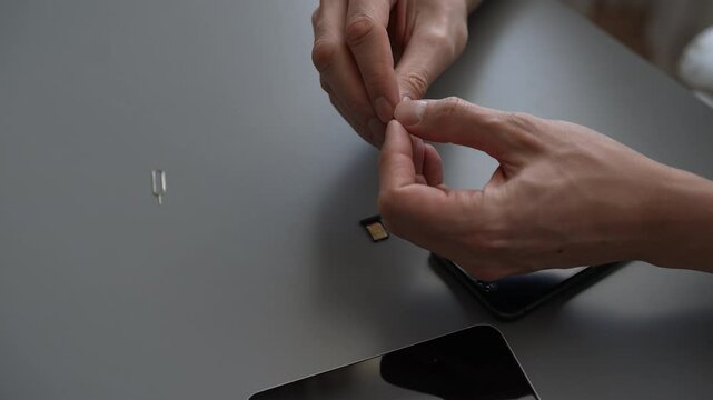 High-angle view of unrecognizable man using sim ejector tool to remove or insert nano sim card from smartphone or tablet. Process of changing mobile service providers or upgrading devices, close-up.
