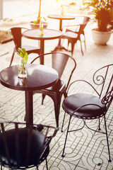 Sunlit outdoor café setting with empty metal tables and chairs